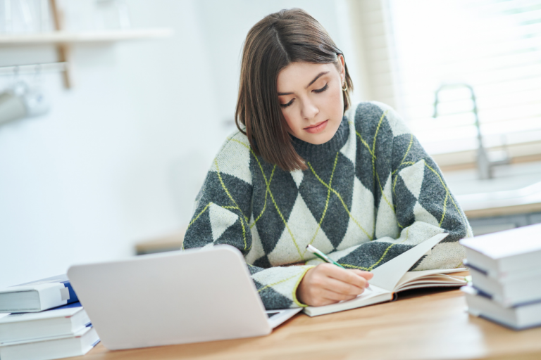 Girl reading book at a desk with a computer on it.