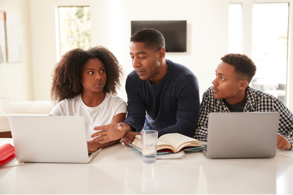 Father talking with two teens with computers.
