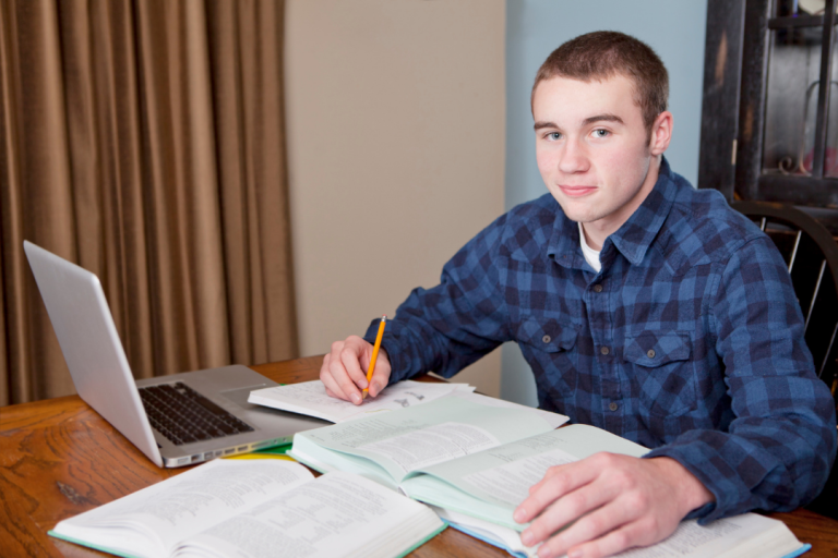 Student comparing information on a laptop with an open reference book and handwritten notes.